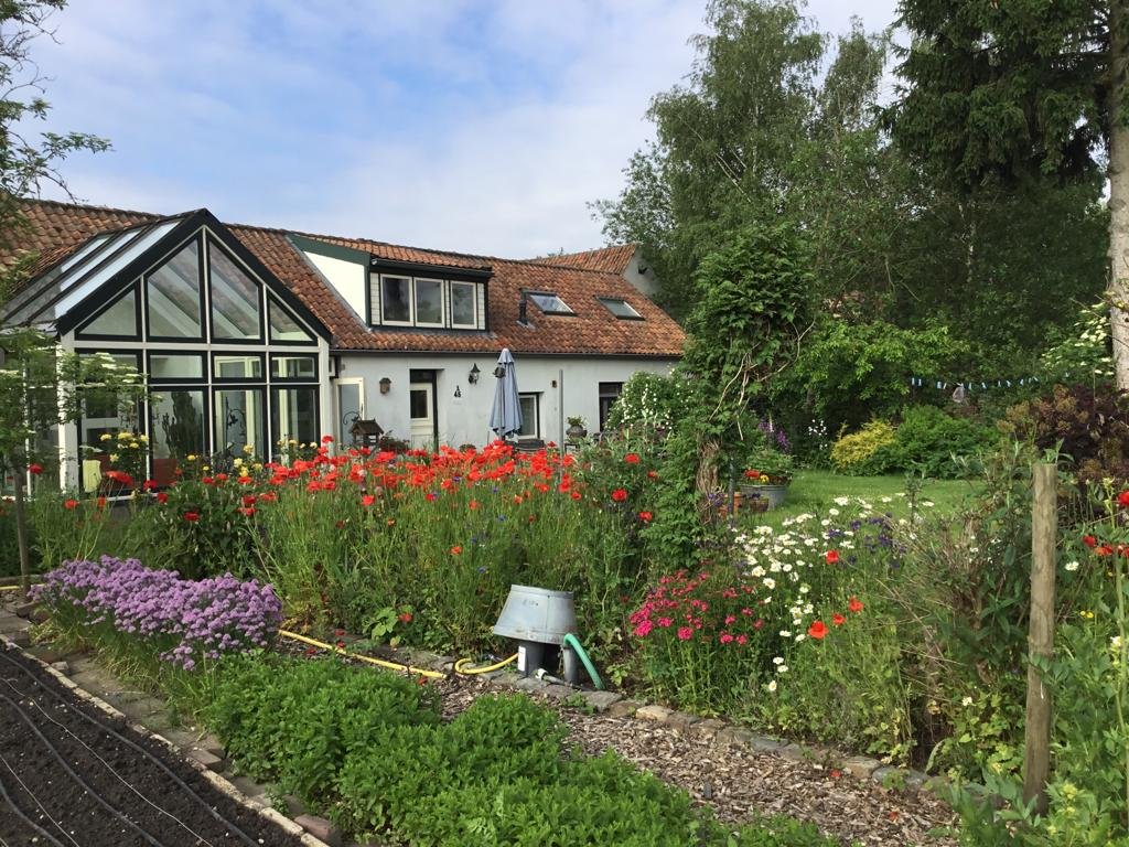 De bloemen- en moestuin van de Genrayhof met het huis en de kas op de achtergrond